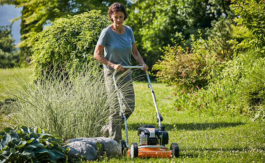 Una mujer corta el césped en un jardín con un cortacésped para mulching STIHL RM 2 R en un jardín en verano.