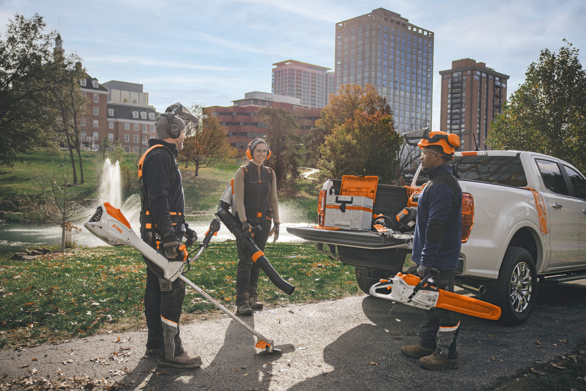 Un grupo de jardineros paisajistas profesionales se reúne alrededor de sus vehículos preparándose para trabajar con herramientas eléctricas a batería STIHL. 