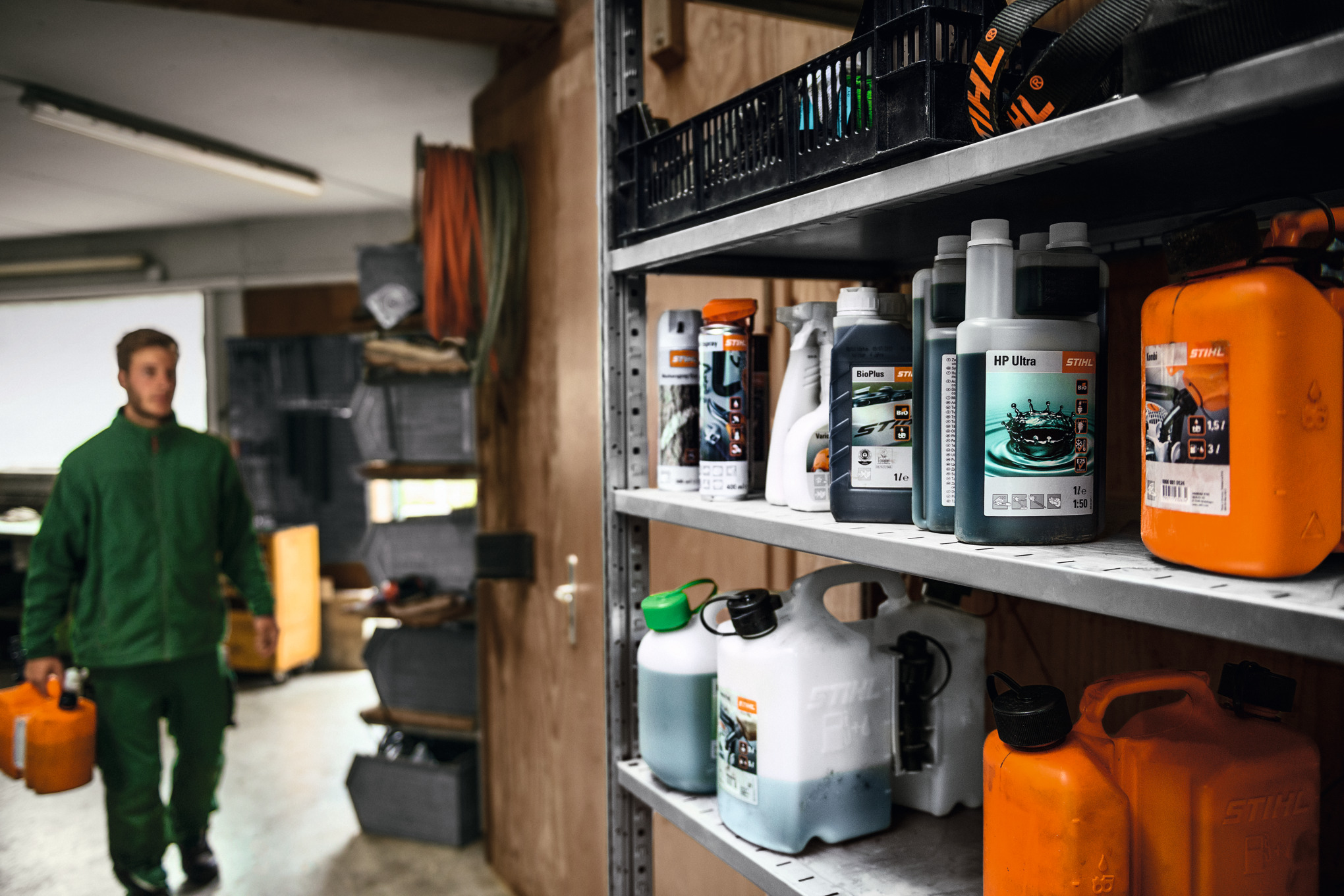 Various STIHL fuels and lubricants on a shelf, with a man in the background holding a canister for transporting hazardous goods 