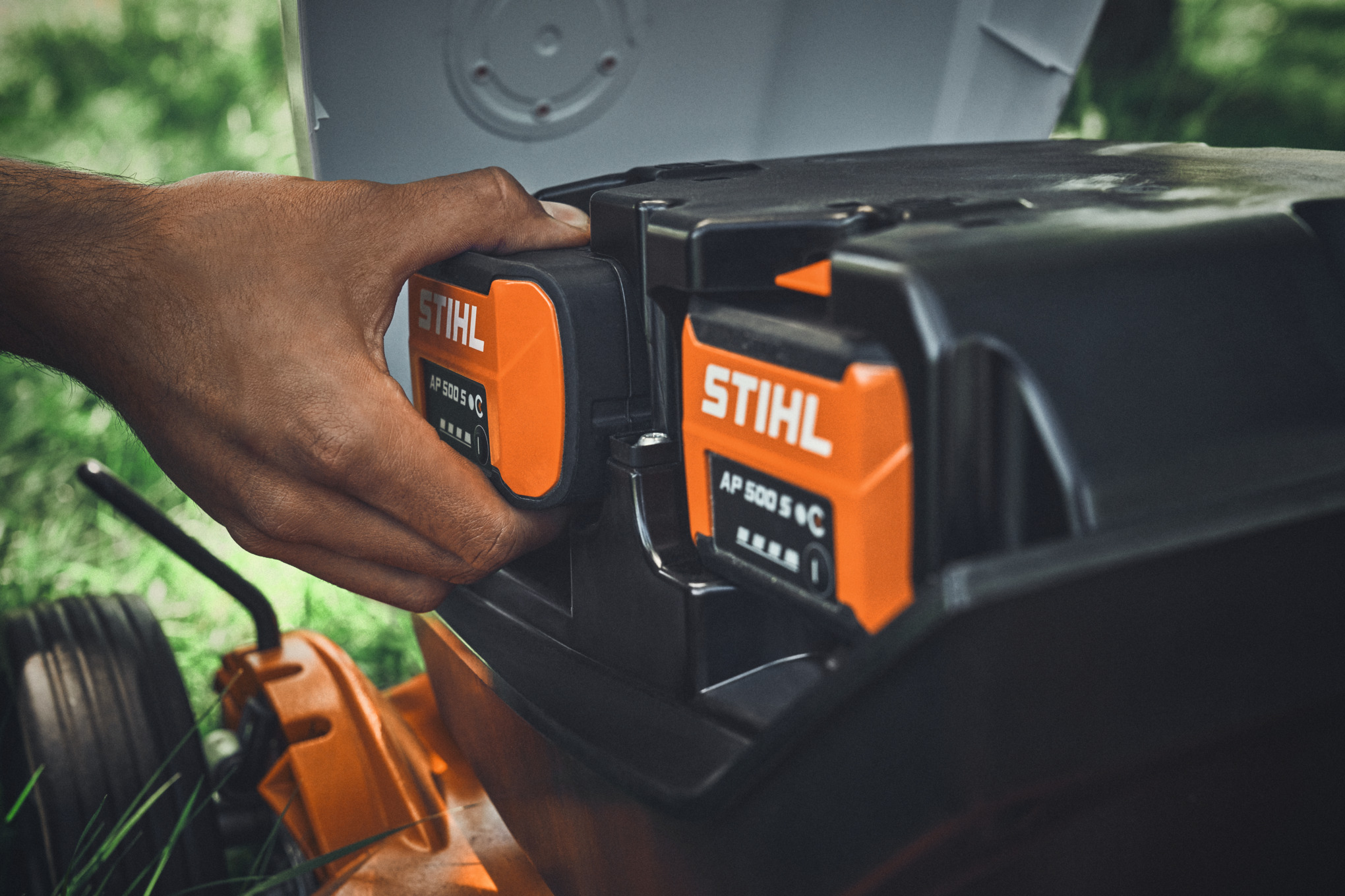 Una persona coloca una batería STIHL AP 500 S en un cortacésped inalámbrico STIHL