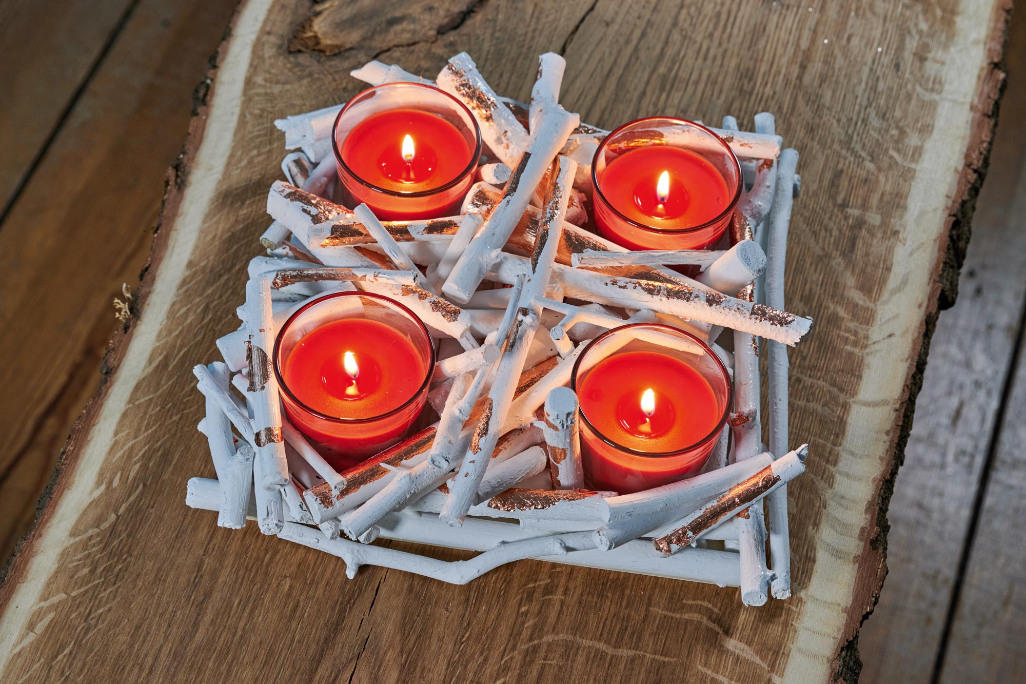 Cuatro velas rojas con portavelas de cristal encendidas en una corona de Adviento artesanal