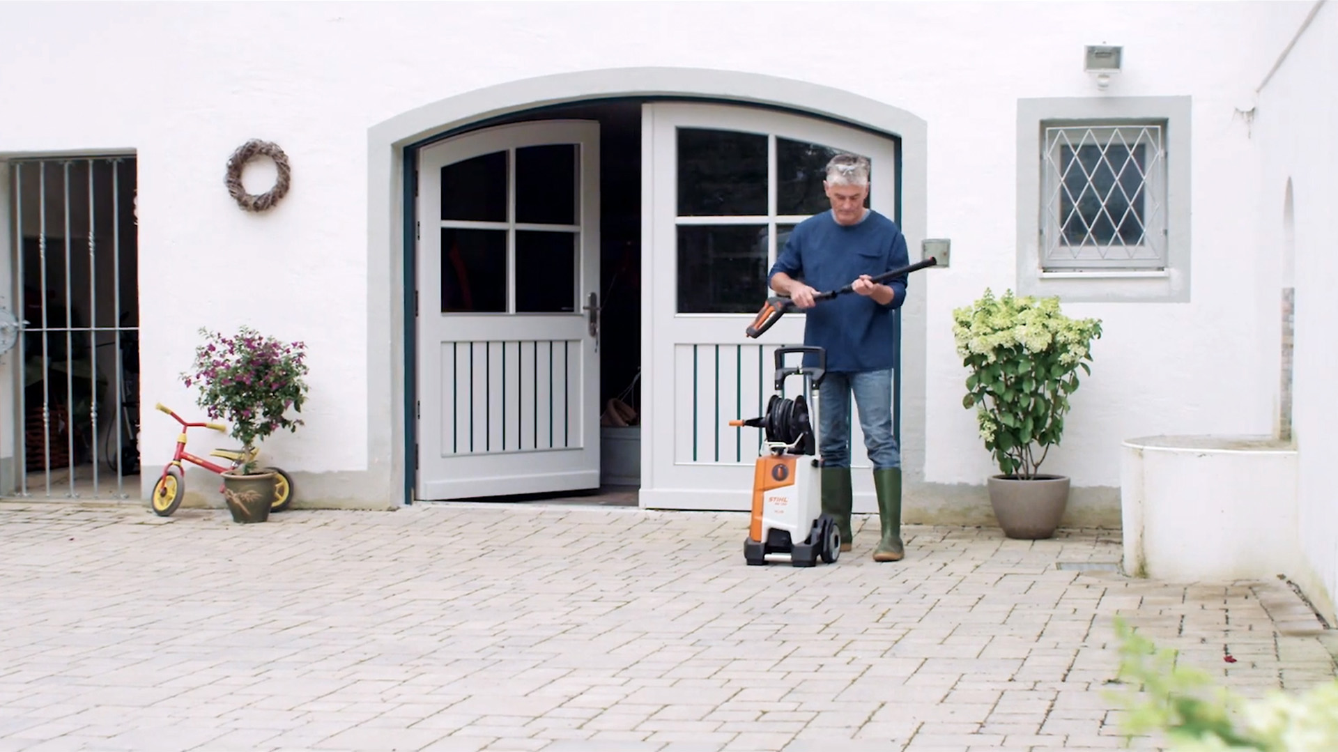 Un hombre delante de una casa preparándose para limpiar las paredes exteriores exteriores con una hidrolimpiadora STIHL