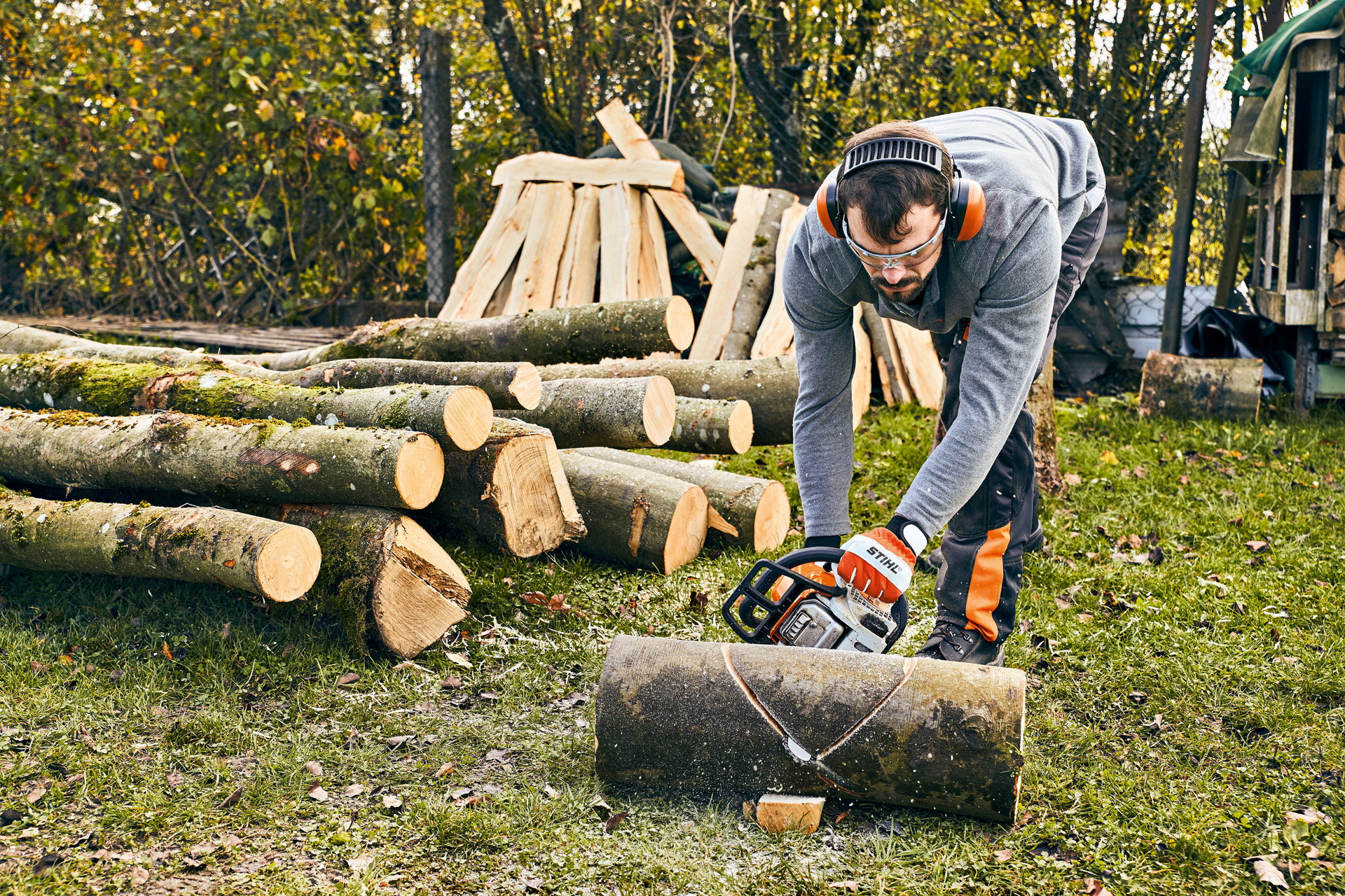 Un hombre con protección auditiva usando una STIHL MS 180 y trabajando en un banco de jardín DIY con una motosierra.