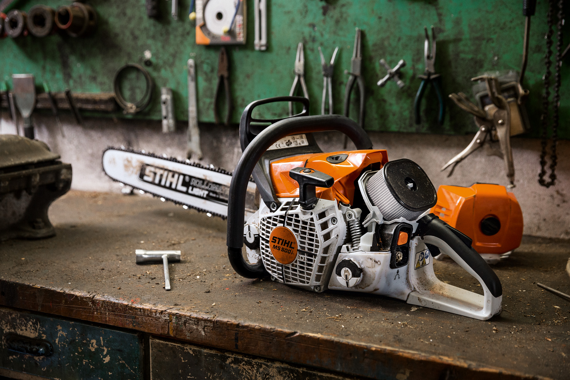 Una motosierra de gasolina STIHL MS 500i W en un banco de trabajo con herramientas colgadas de la pared posterior