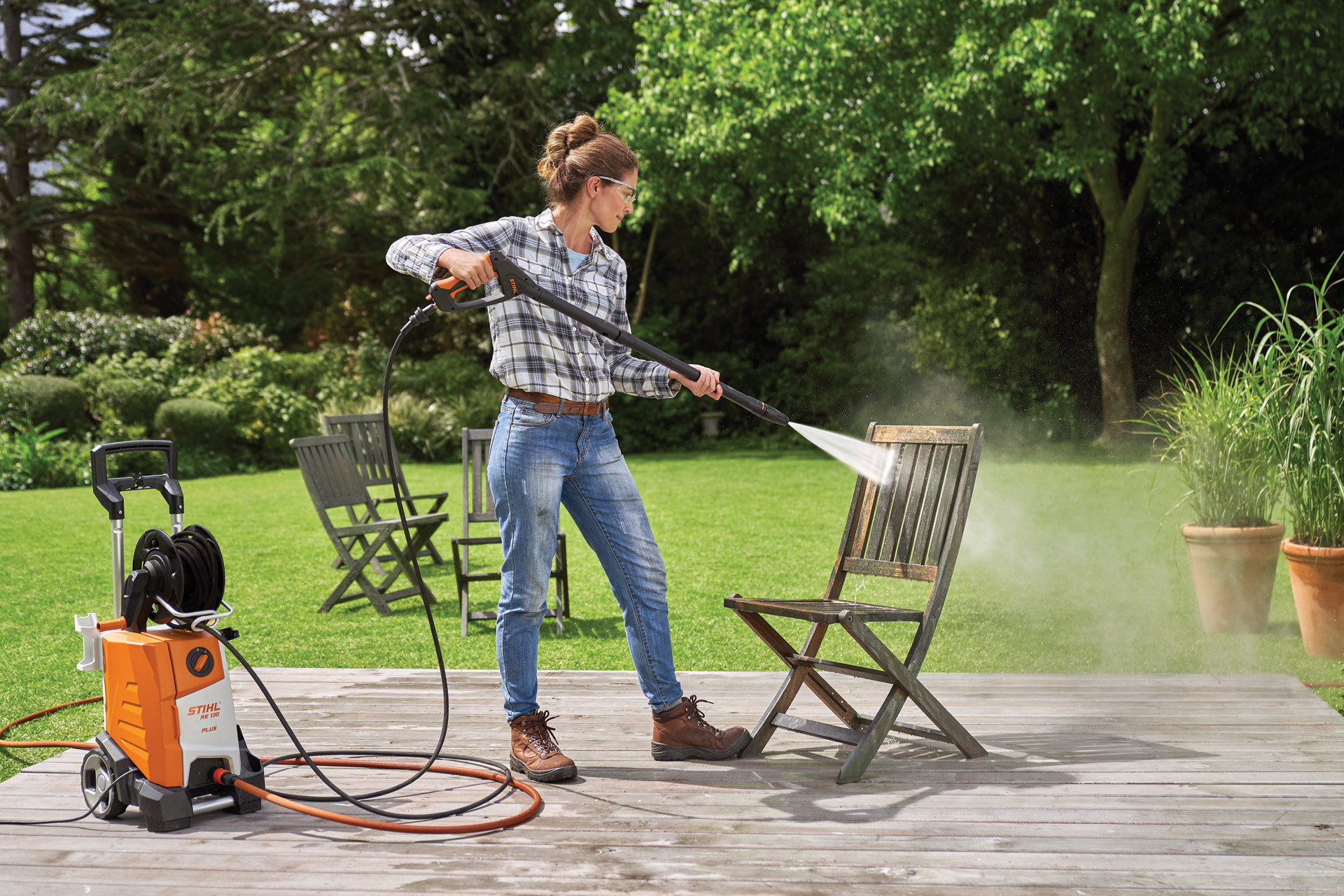 Una mujer sabe cómo limpiar muebles de jardín y aclara una silla con una hidrolimpiadora STIHL RE 130 Plus en un patio.