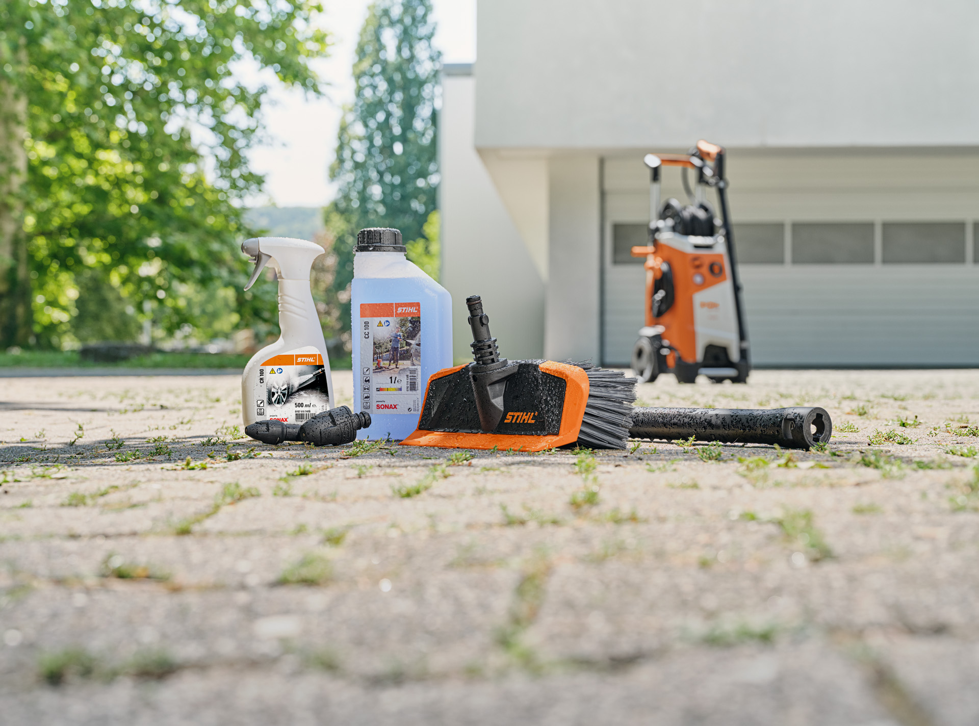  Detergente para llantas, jabón y cepillo de lavado delante de un garaje. En segundo plano, una hidrolimpiadora STIHL.