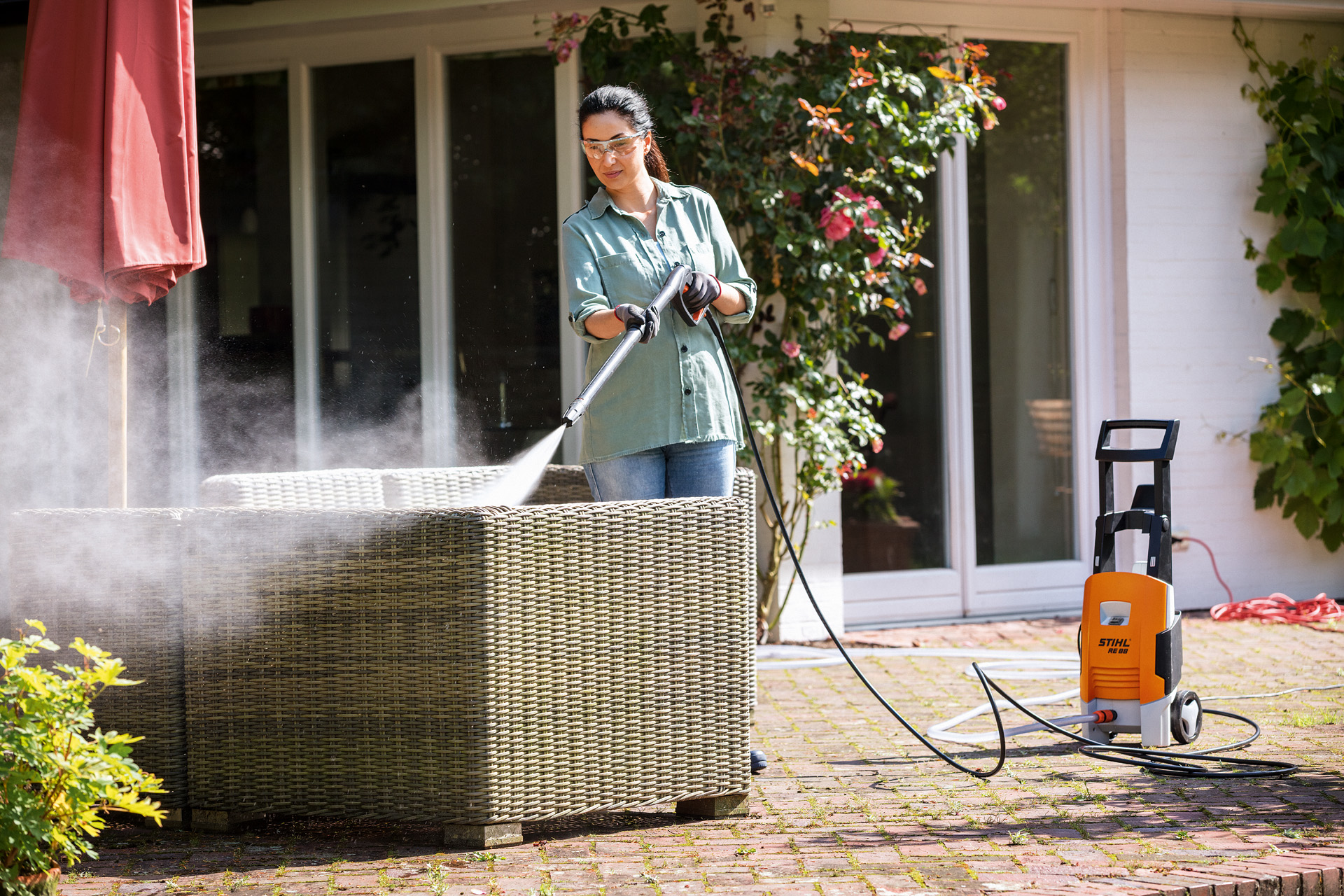 Mujer limpiando sillas de jardín de madera en su terraza con una hidrolimpiadora  STIHL RE 130 plus