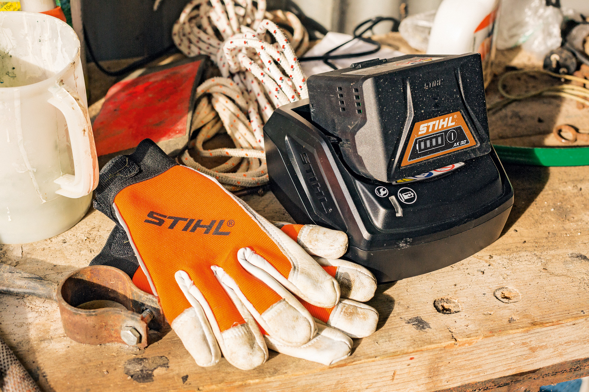 Carga de una batería de litio de la serie STIHL AK situada al lado de unos guantes en una mesa de madera