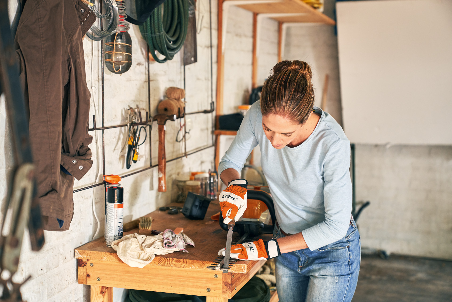 Mujer con guantes de protección sabe cómo afilar un cortasetos STIHL usando una lima plana para afilar un cortasetos