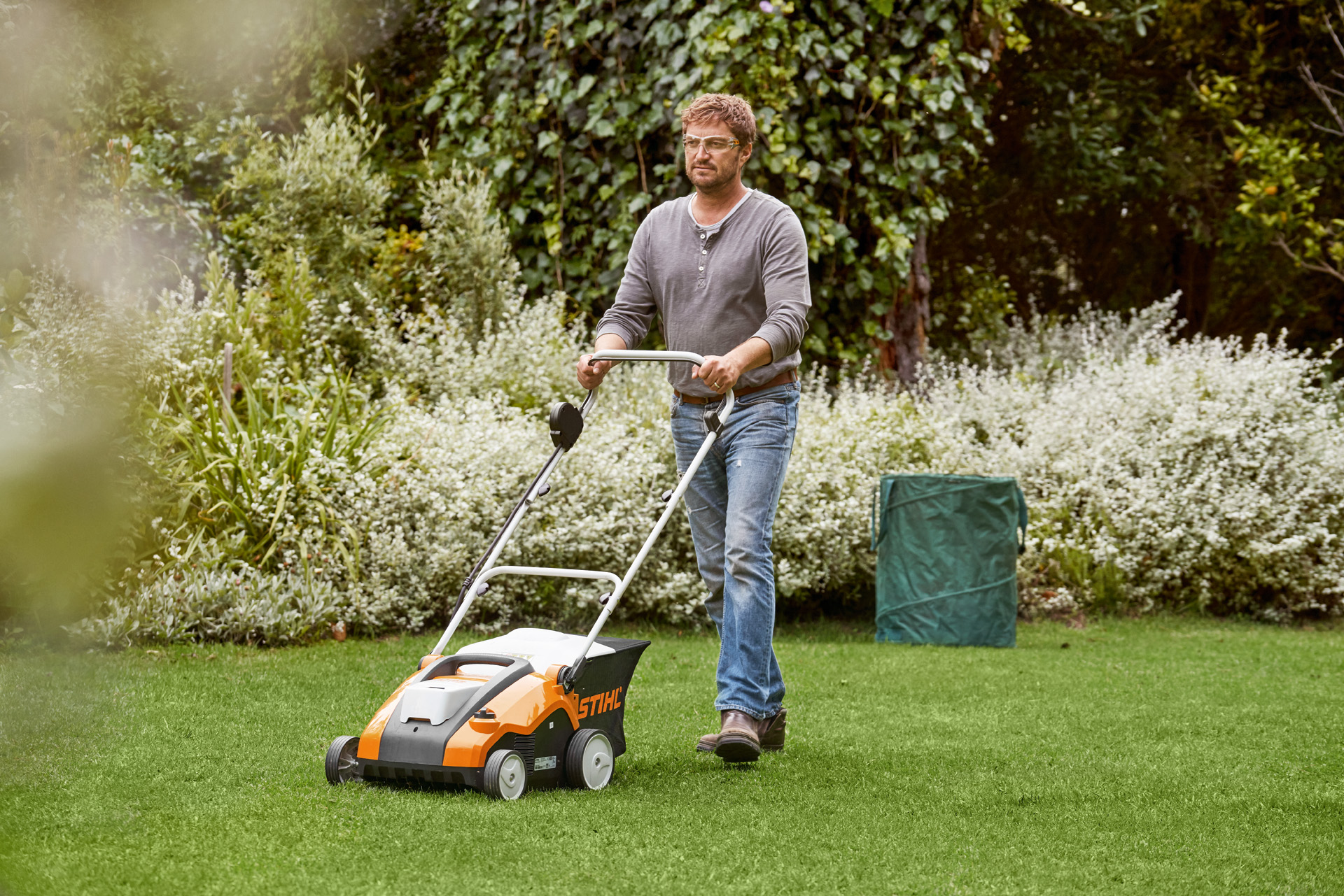 Un hombre escarifica un césped verde con un STIHL RLA 240.