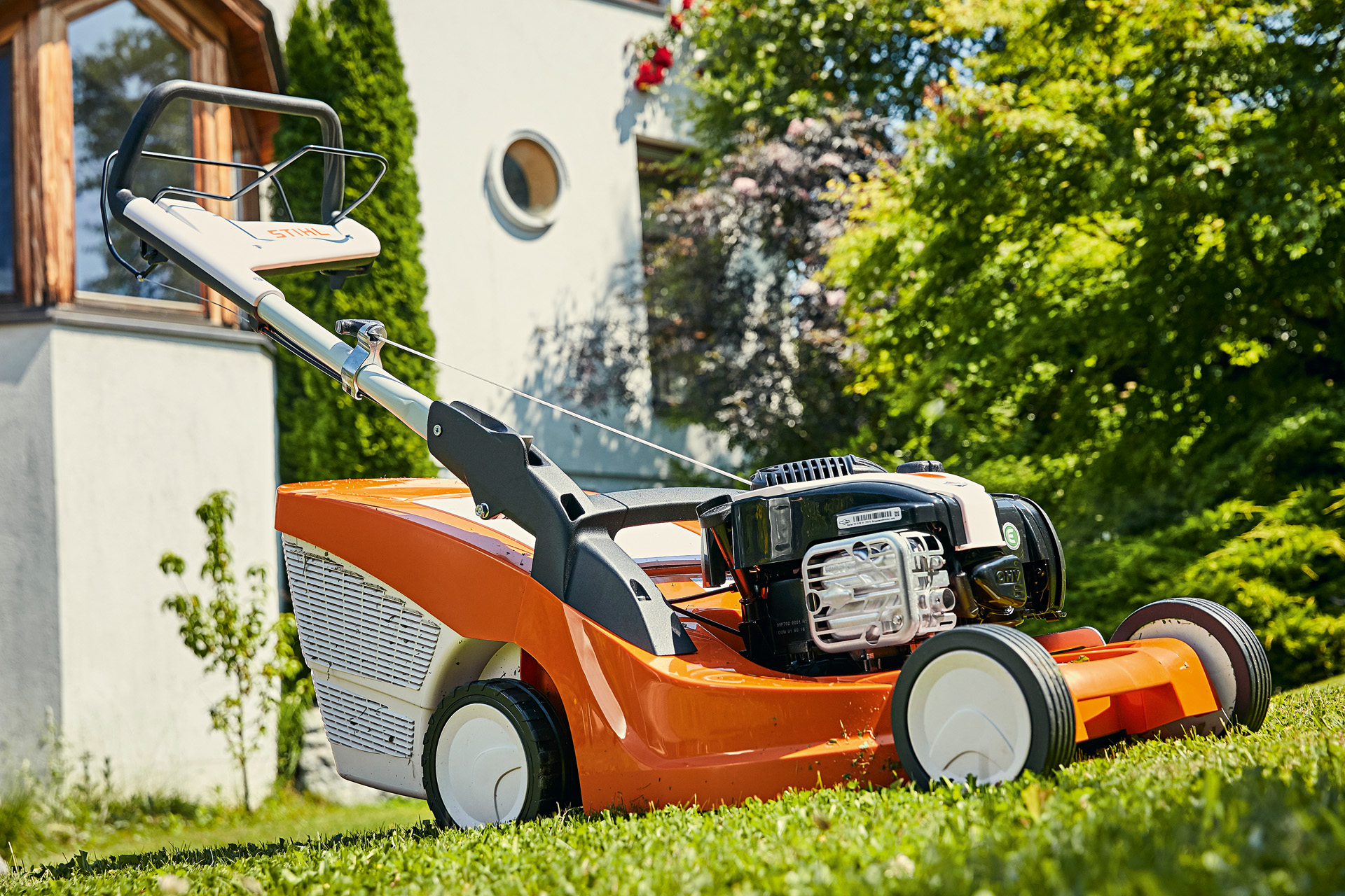 Un cortacésped de gasolina STIHL RM 443 T en un jardín con una casa de fondo