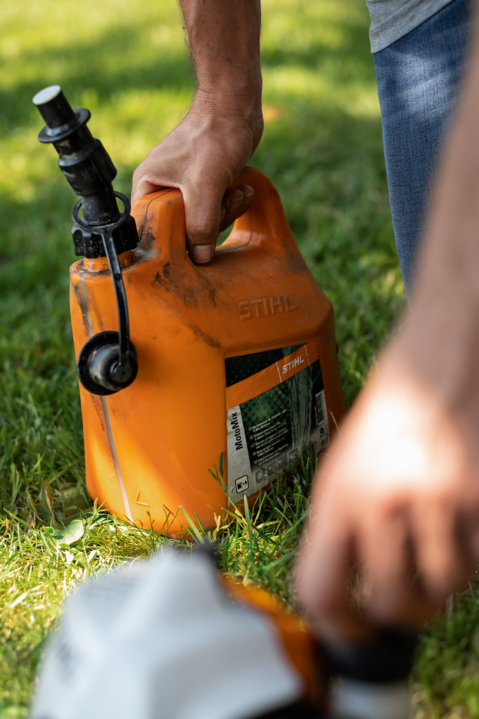 Recipiente abierto de combustible STIHL MotoMix y, en primer plano, una mano abriendo la tapa del combustible.