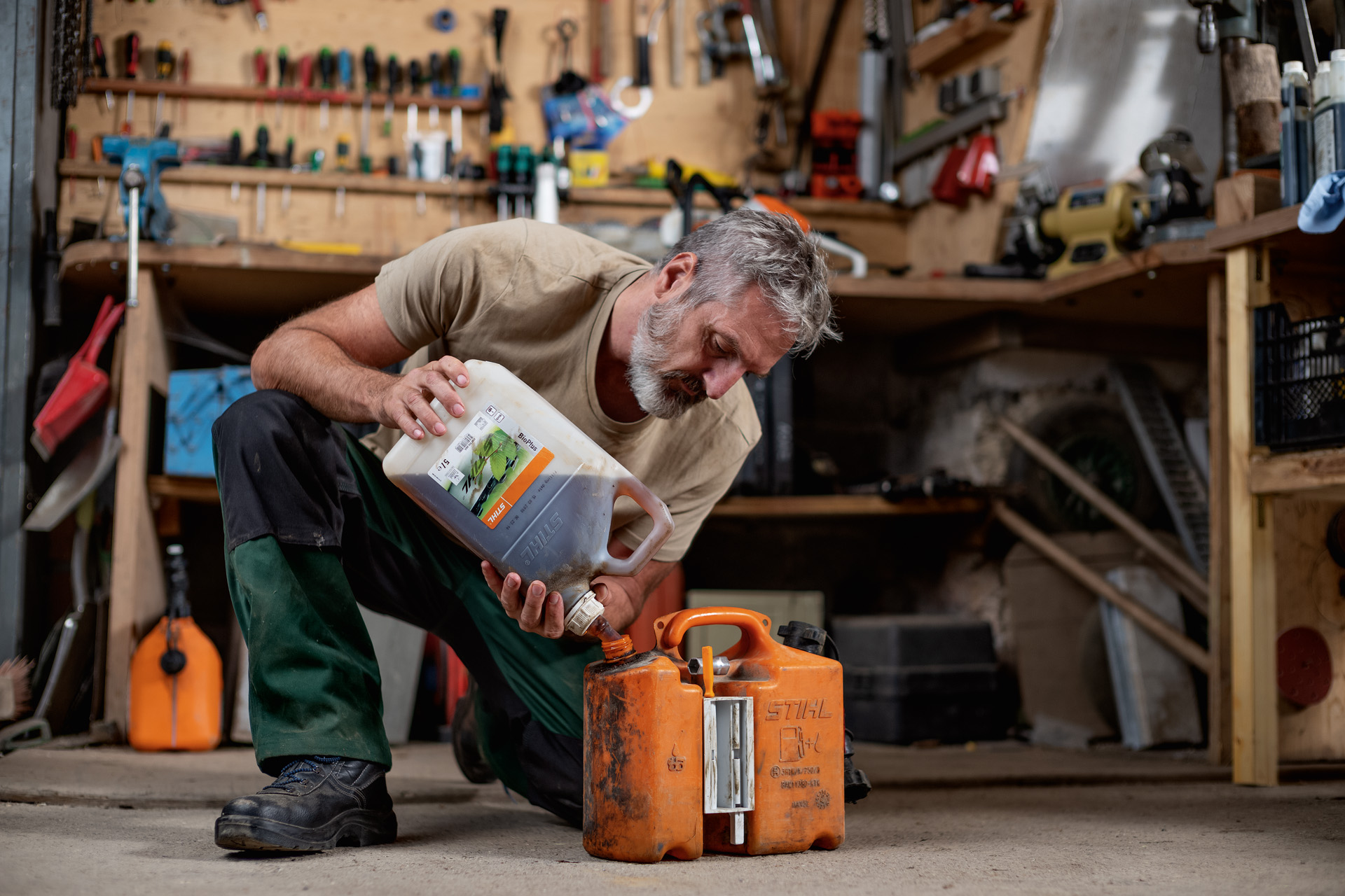 Un hombre arrodillado llena un recipiente naranja con combustible STIHL