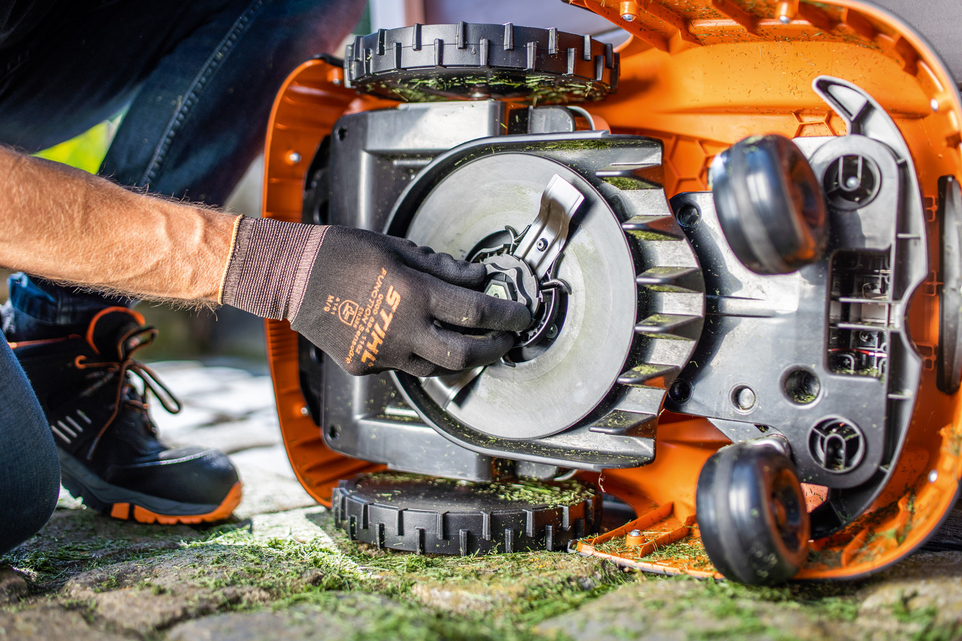 Vista de la parte inferior limpia de un robot cortacésped STIHL iMOW® y una persona con guantes comprobando la cuchilla
