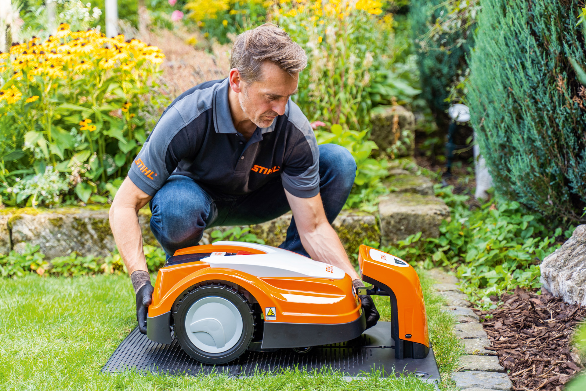 Un distribuidor STIHL coloca un robot cortacésped iMOW de STIHL en una estación de carga en un jardín
