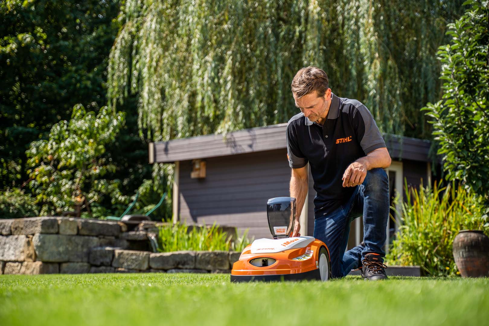 Un distribuidor STIHL arrodillado configurando el plan de corte de un robot cortacésped STIHL RMI 422 iMOW® en un jardín