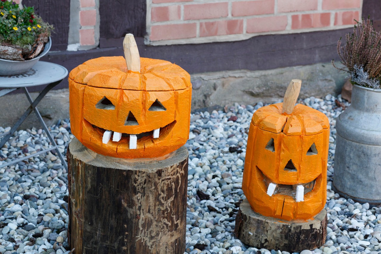 Manualidades de Halloween: un par de calabazas decorativas de madera en un jardín.