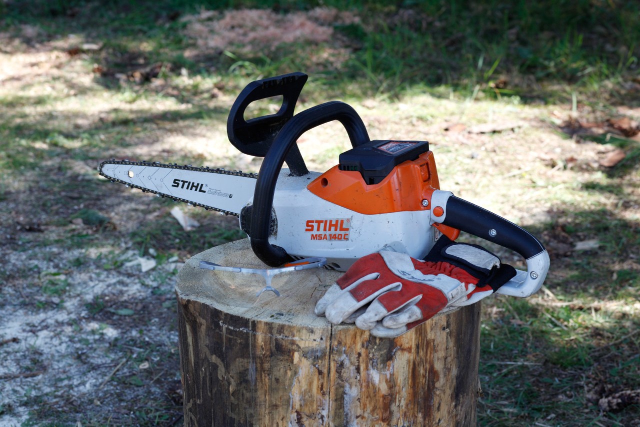 Motosierra de batería STIHL MSA 140 C y guantes de protección en un tocón de árbol
