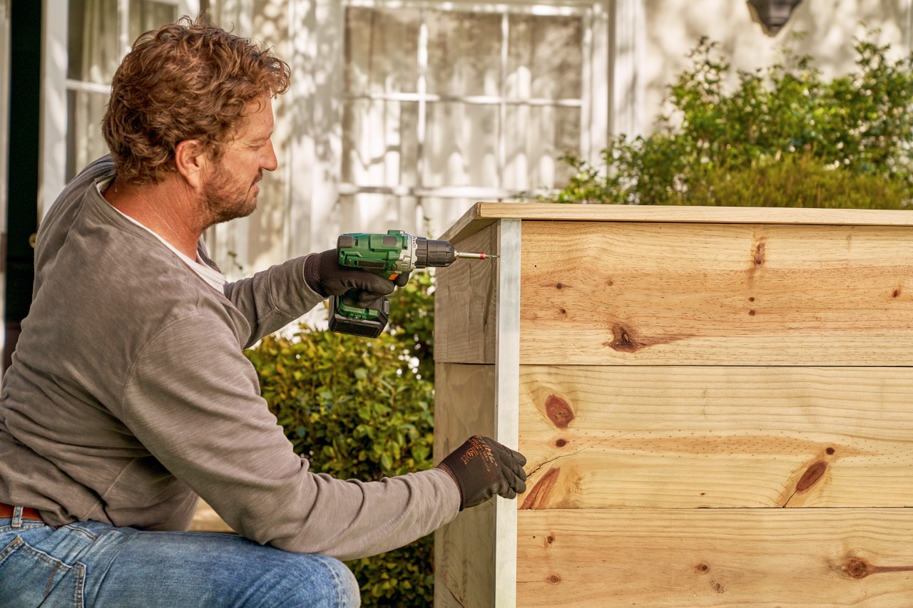 Construir una mesa de cultivo: un hombre atornillando el ángulo de aluminio al borde exterior de la mesa de cultivo.