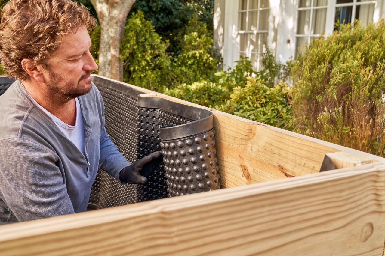 Construir una mesa de cultivo DIY: un hombre fijando la membrana impermeable negra en el interior de la mesa.