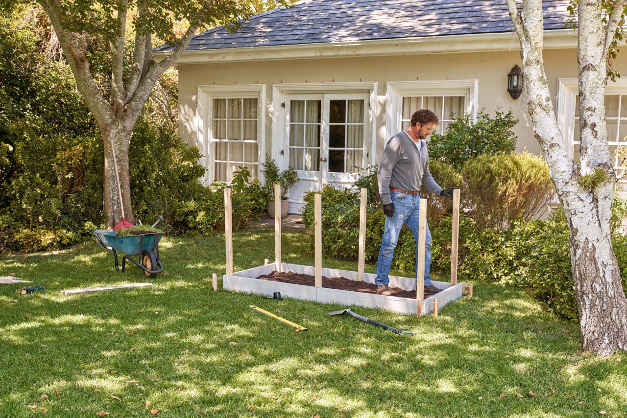 Construir una mesa de cultivo DIY a partir de tableros: un hombre de pie entre los postes de refuerzo.