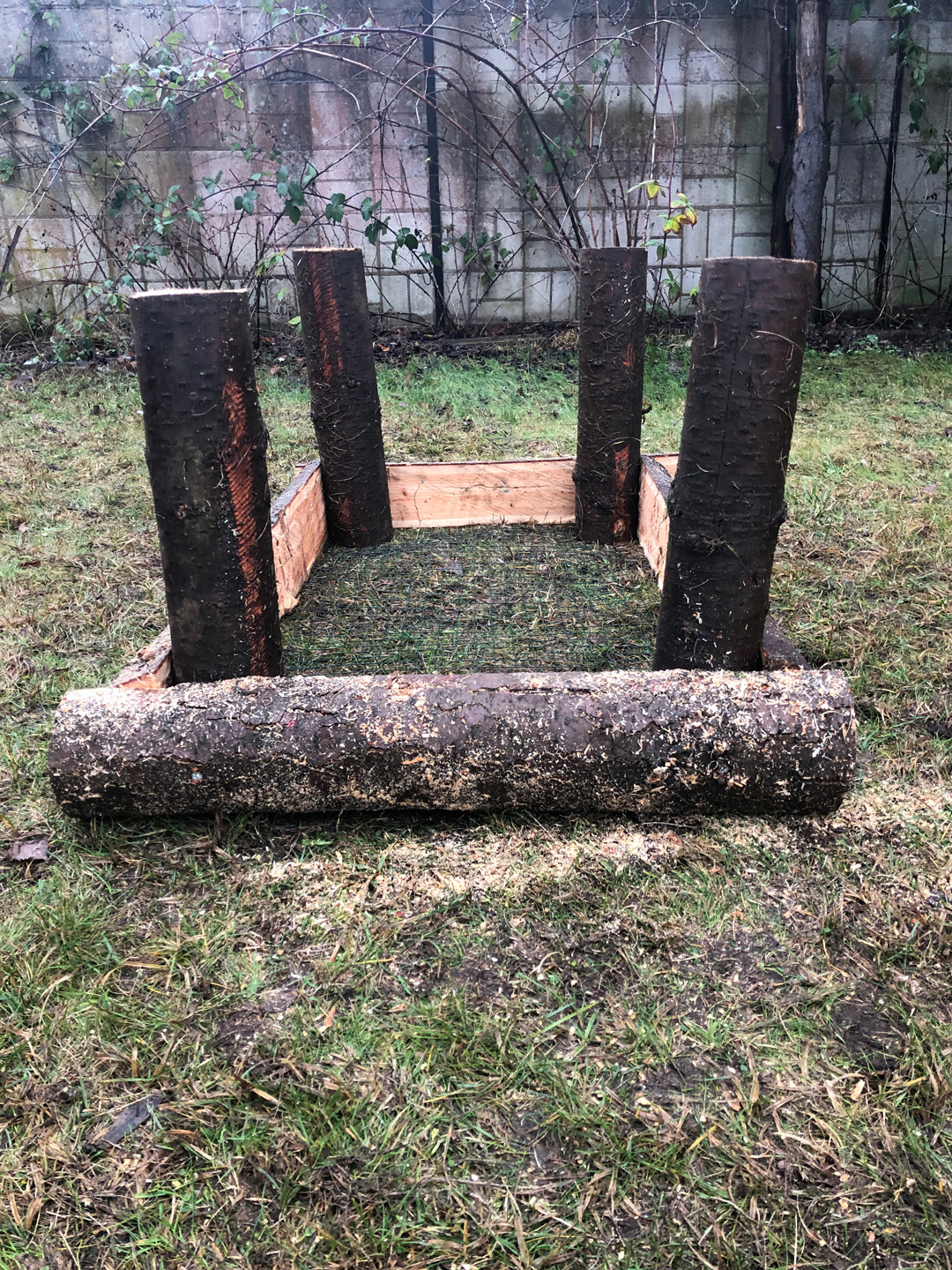 Base de una mesa de cultivo, con cuatro postes verticales formando un rectángulo y una fila de troncos bien divididos.