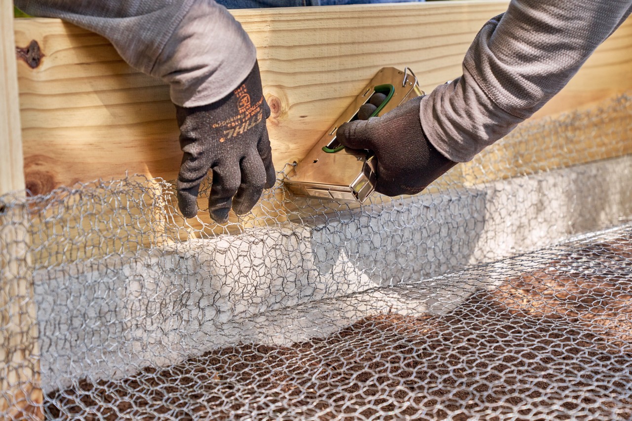 Construir una mesa de cultivo DIY a partir de tableros: malla de alambre grapada a un tablero dentro de la mesa.