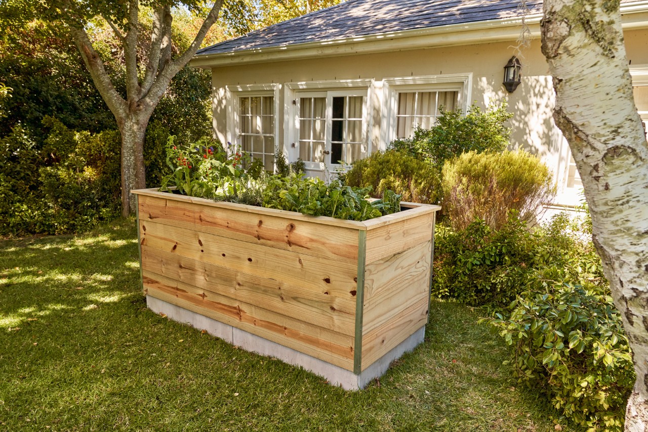 Mesa de cultivo hecha con listones de madera, en el jardín frente a una casa.