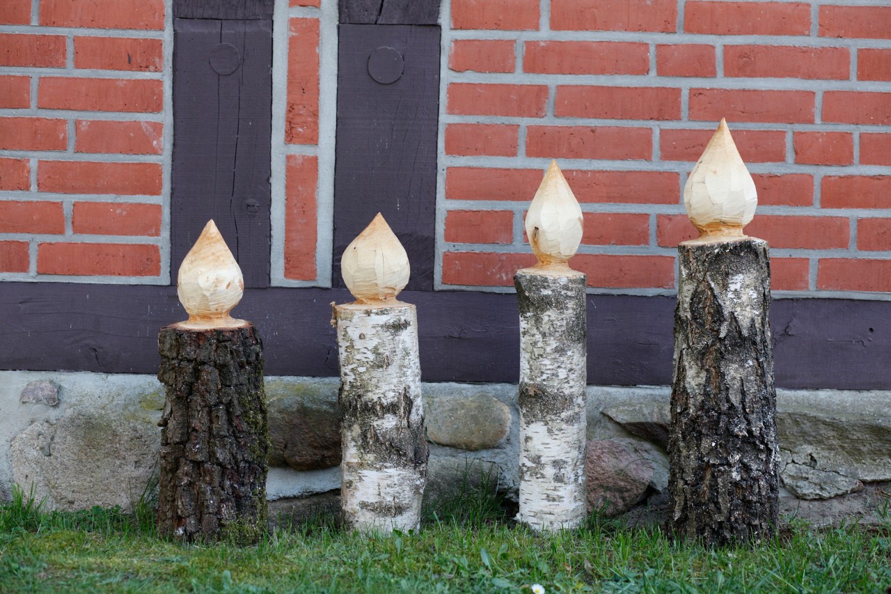 Crea tus velas de madera: Cuatro velas de pie sobre el césped frente a una pared de ladrillos rojos