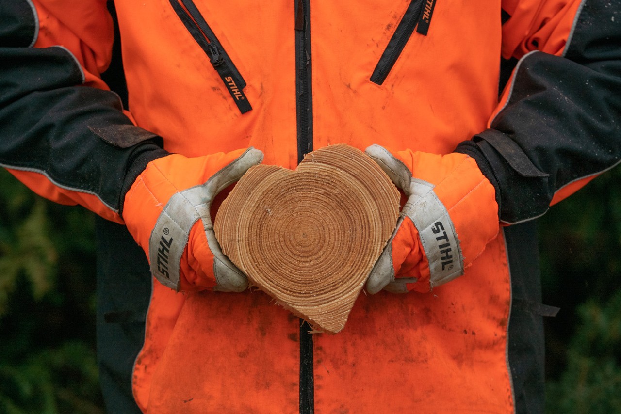 Una persona con ropa de protección sostiene un corazón tallado con motosierra en madera.