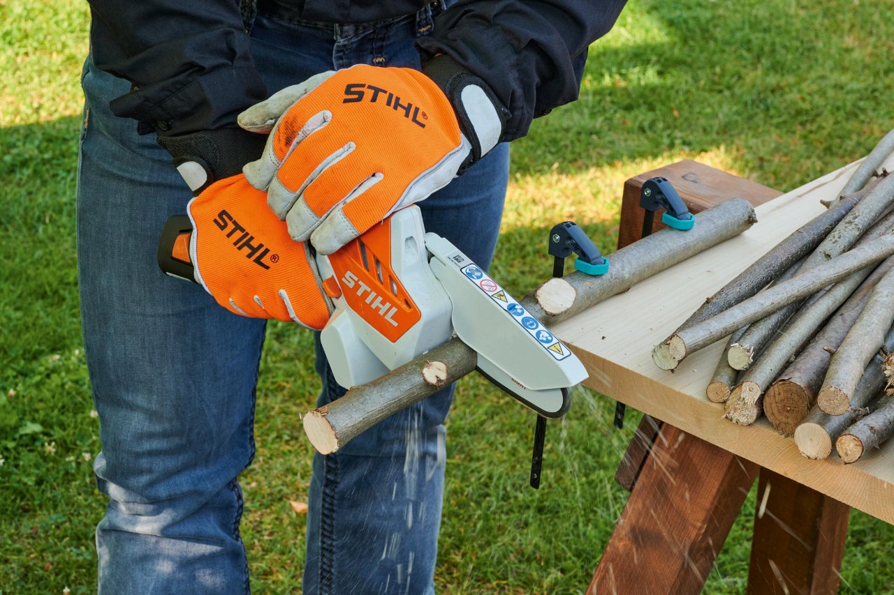 Crea tus coronas de Adviento artesanales: una persona con guantes anticorte cortando ramas en piezas cortas con una minisierra de batería STIHL GTA 26
