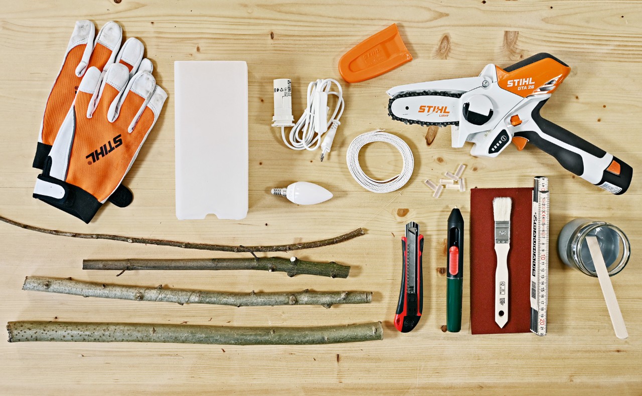 Materiales para hacer una lámpara de mesa a partir de ramas: guantes, minisierra de batería STIHL GTA 26, y ramas.