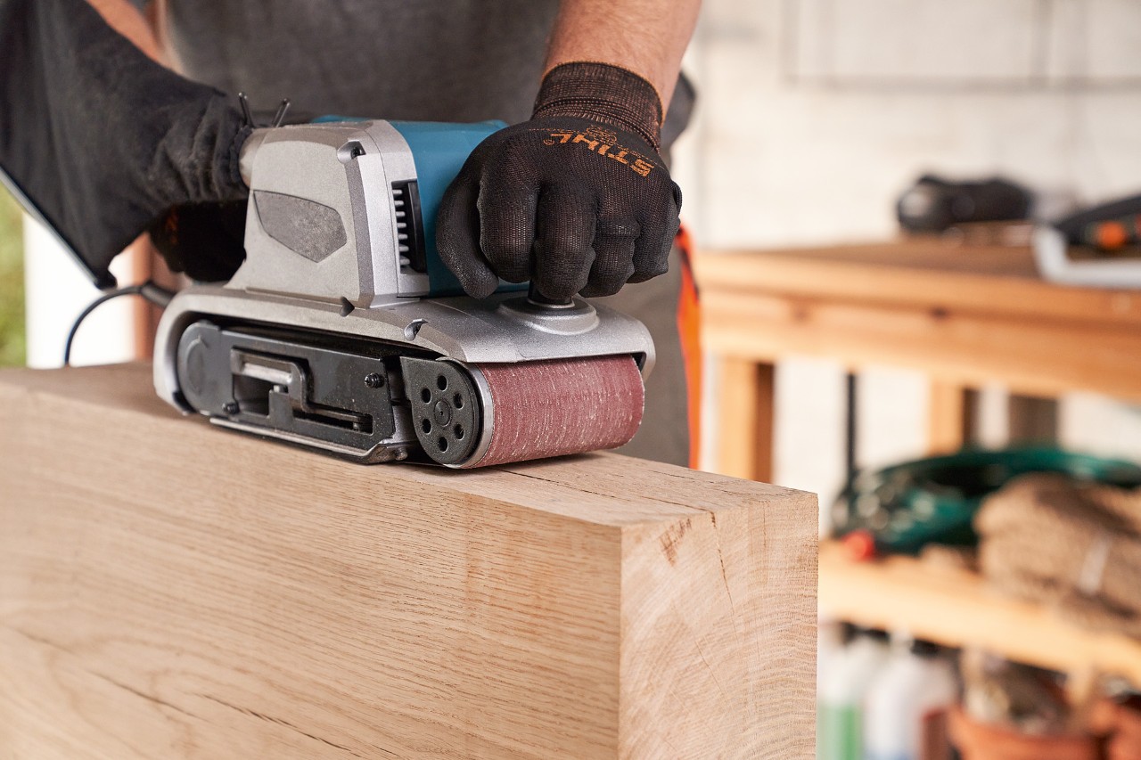 Una persona con guantes de protección lijando madera con una lijadora en el taller