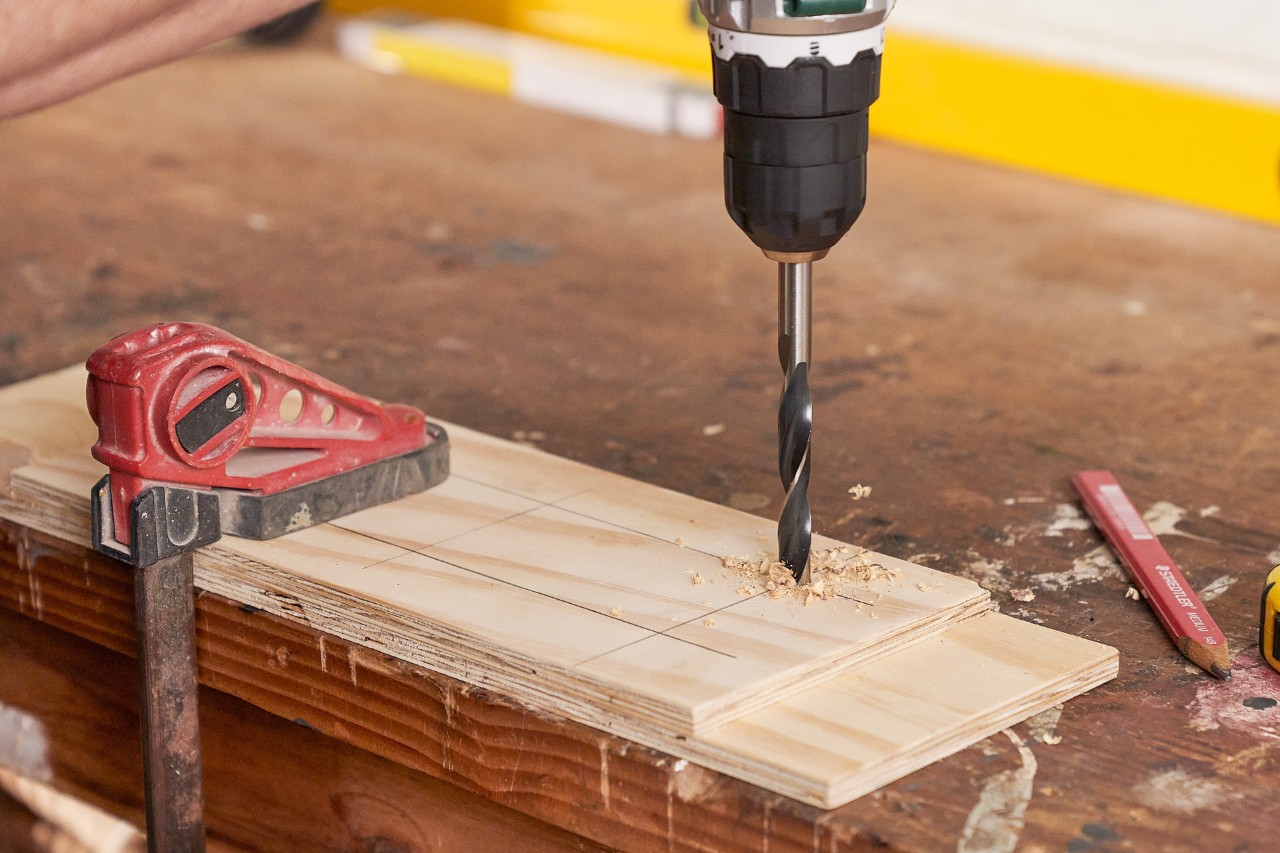 Destornillador de batería haciendo un agujero en una tabla de madera fina para preparar una plantilla de perforación