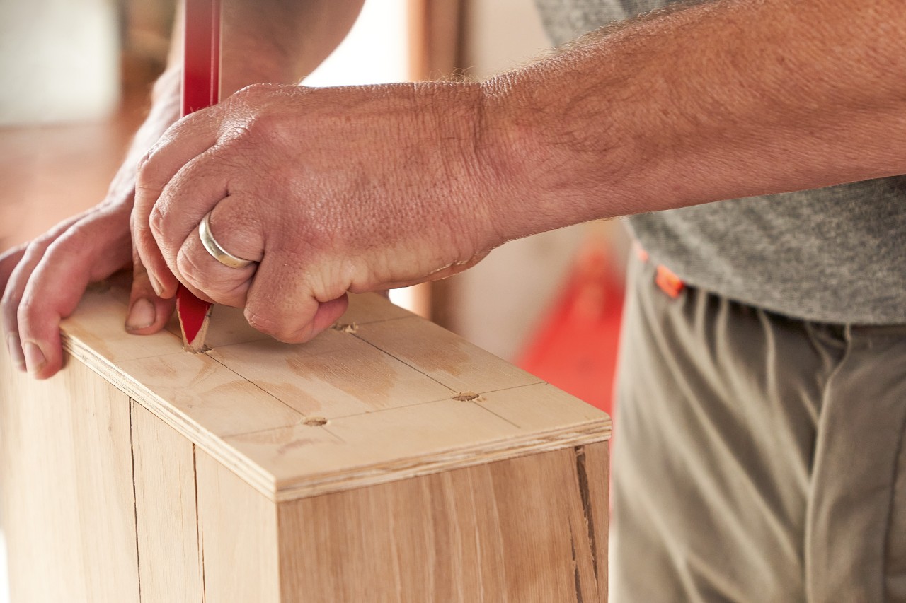 Un hombre marca los puntos de perforación en una viga de madera con ayuda de una plantilla de perforación