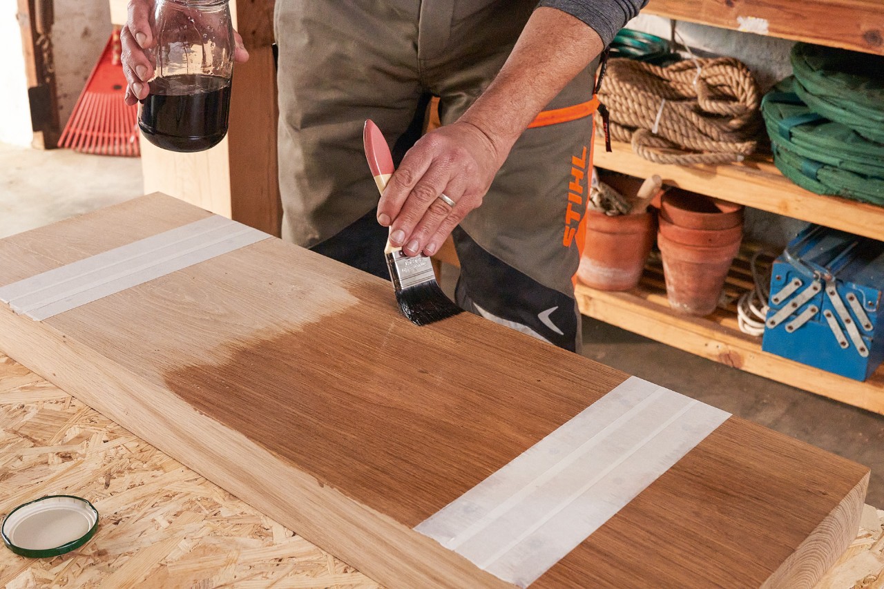 Un hombre con pantalón con protección anticorte STIHL lubrica una viga de madera con un pincel