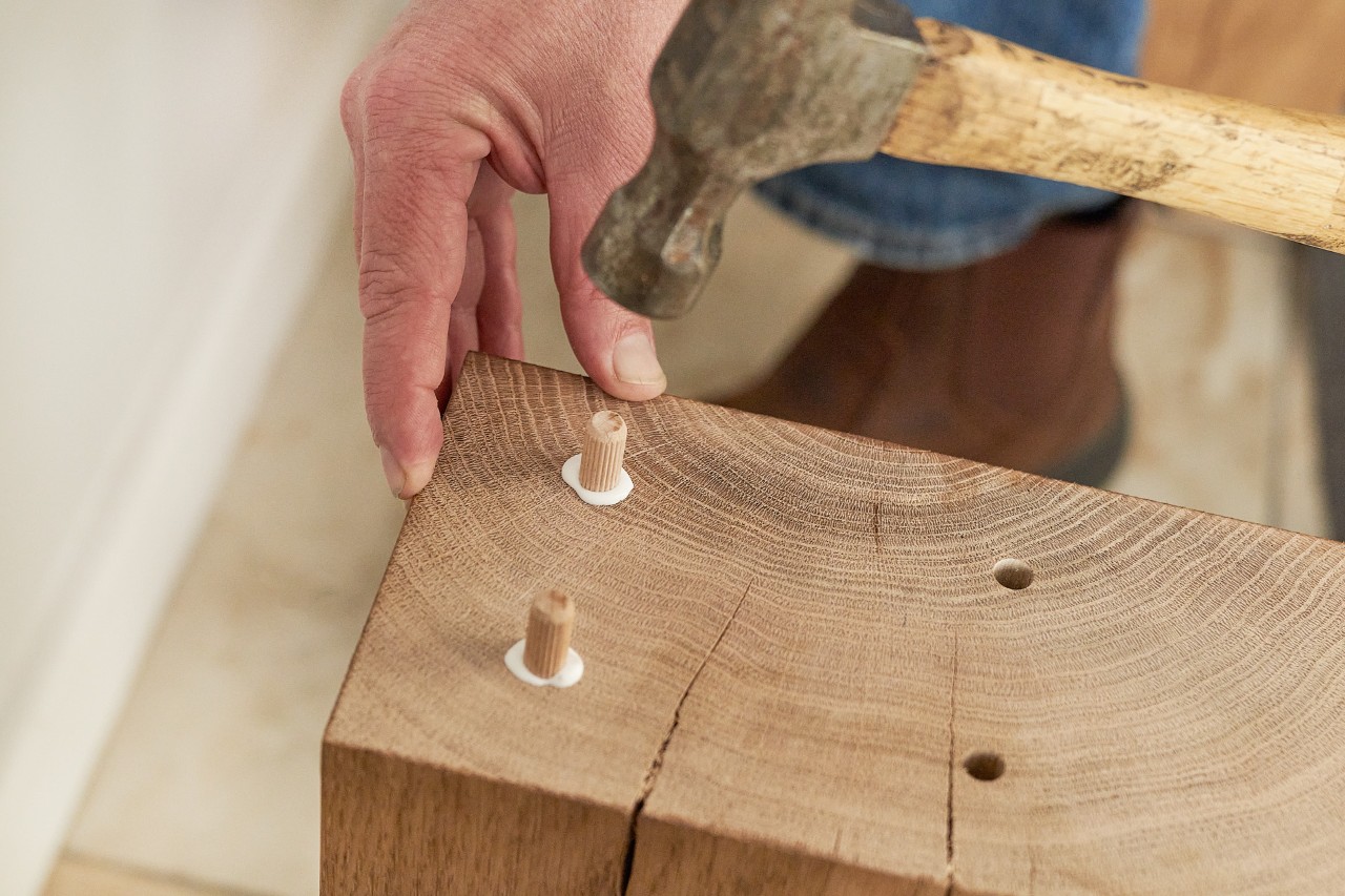 Una persona clava tacos en una viga de madera con el martillo 