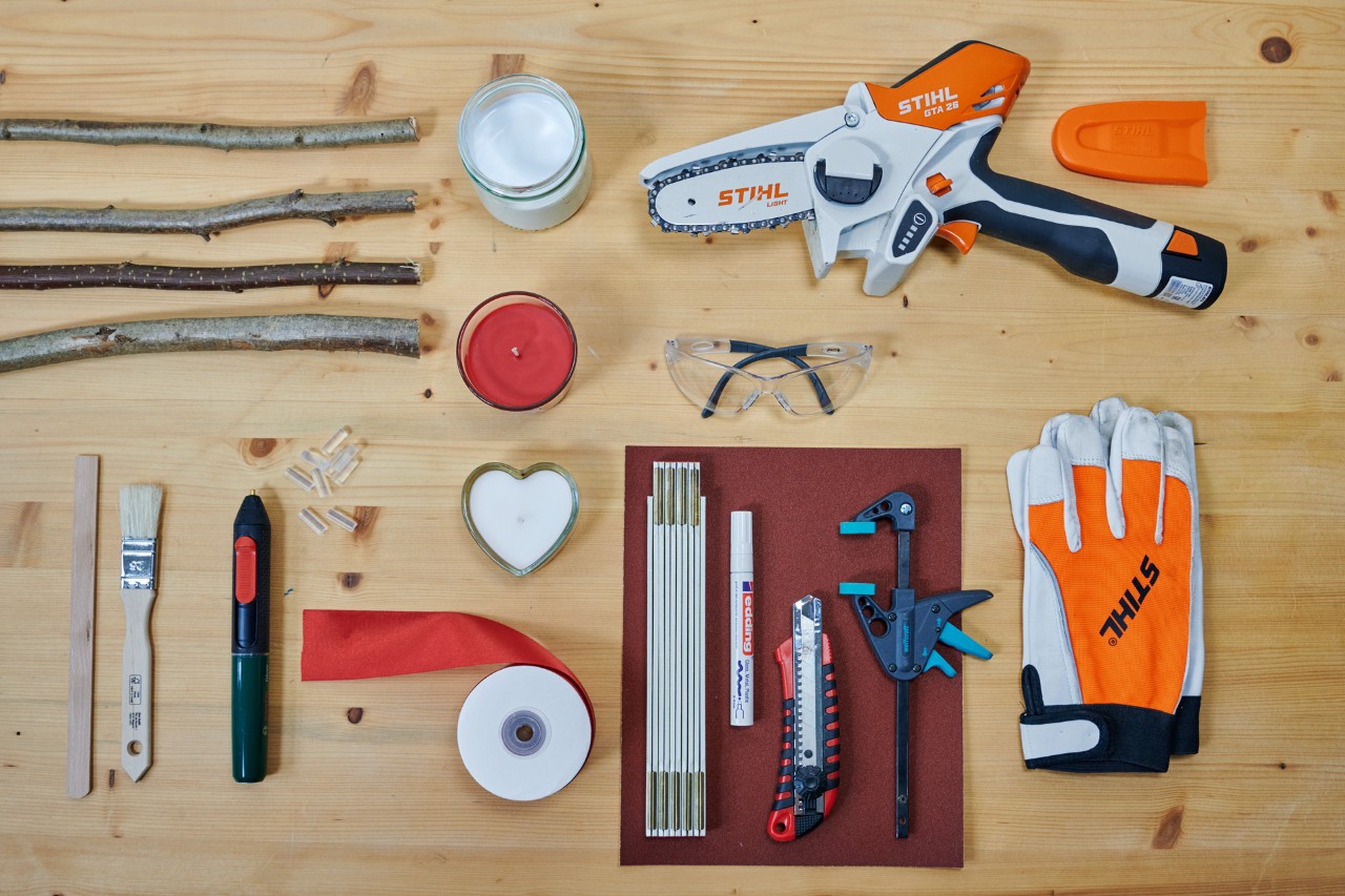 Crear un corazón con ramas secas: minisierra de jardín STIHL GTA 26, guantes, ramas, un cuchillo y velas con soporte.