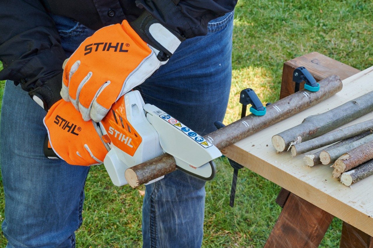 Crear un corazón de ramas: una minisierra de batería STIHL GTA 26 se utiliza para cortar una rama sujeta a una mesa.