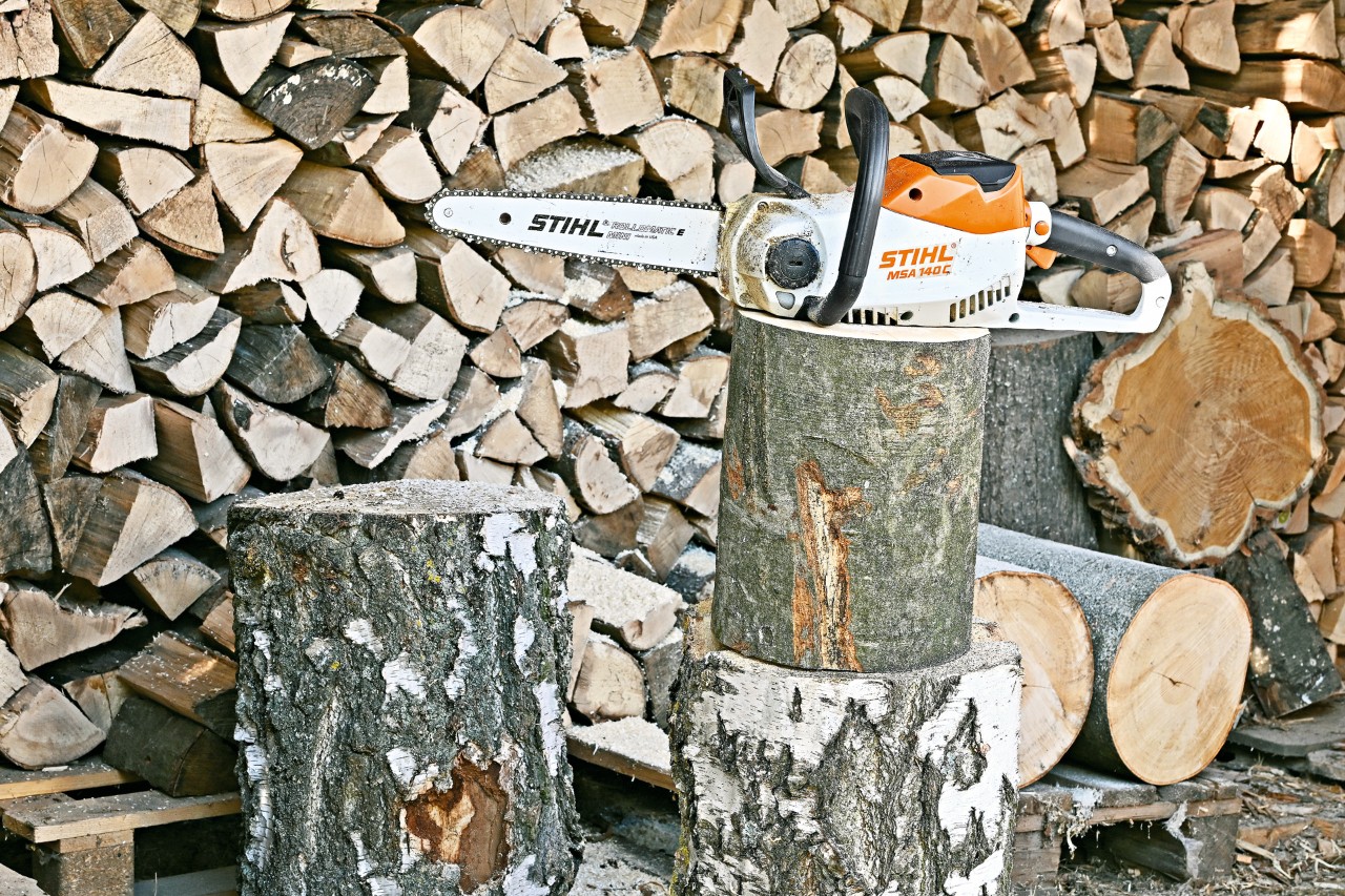 Una motosierra de batería STIHL MSA 140 C en un tocón de árbol delante de una pila de troncos.