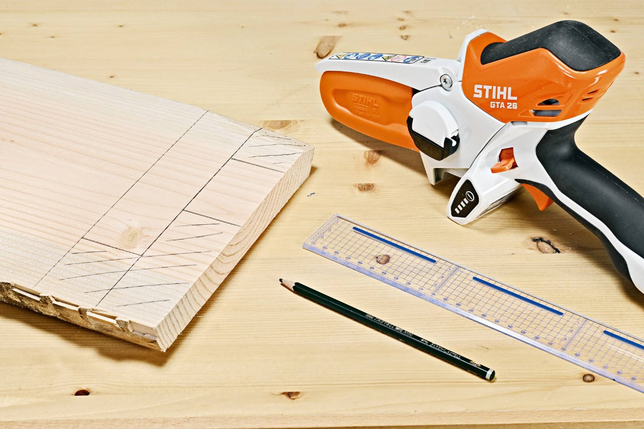 Marcas de lápiz en una tabla de madera junto a una minisierra de batería STIHL GTA 26, un lápiz y una regla.