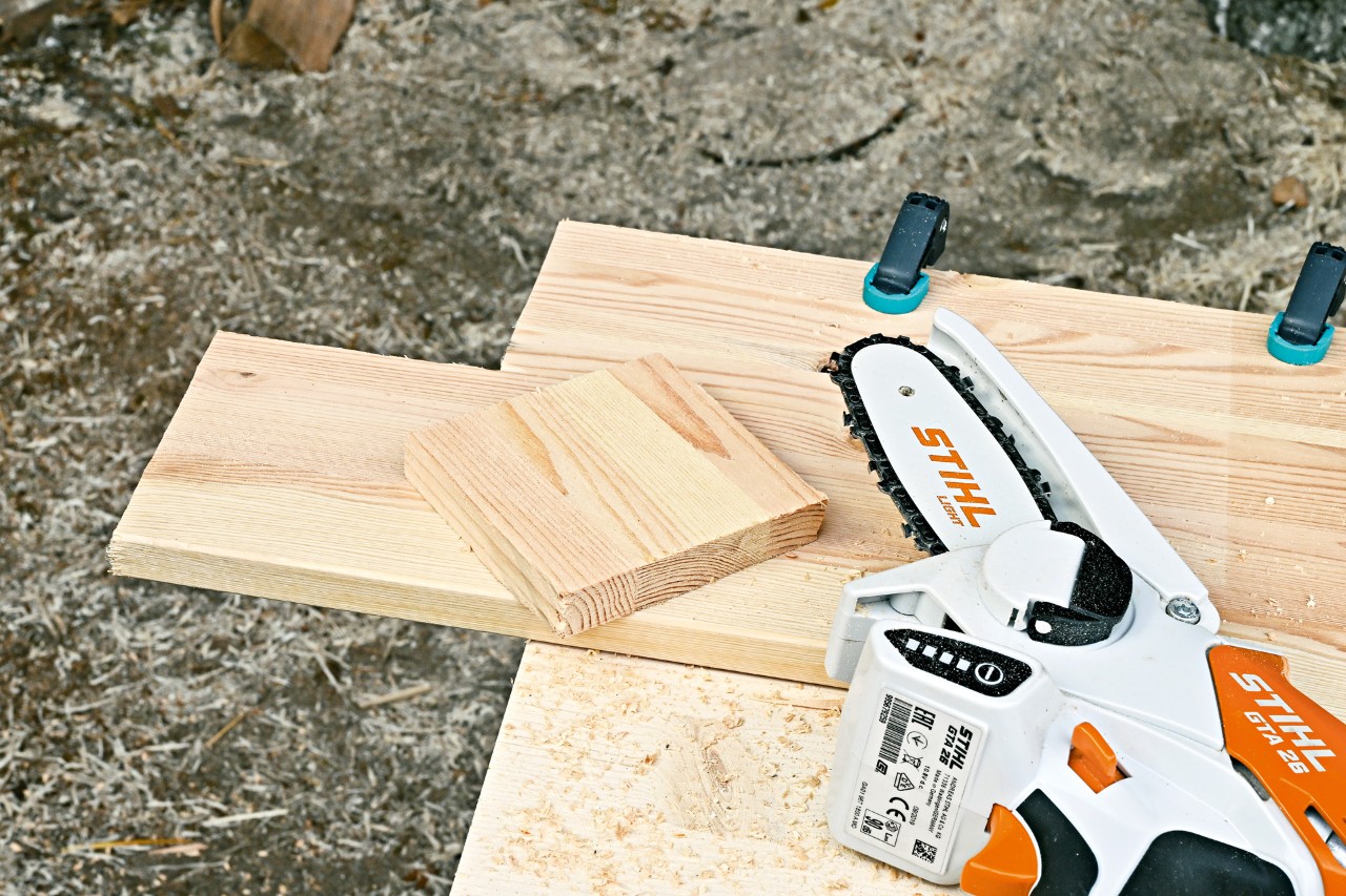Minisierra de batería STIHL GTA 26 junto a un trozo de madera en el que se ha cortado un cuadrado.