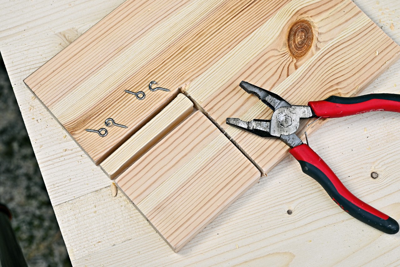 Cuatro hembrillas y unos alicates en una tabla de madera a la que se le ha cortado una parte para hacer la puerta.