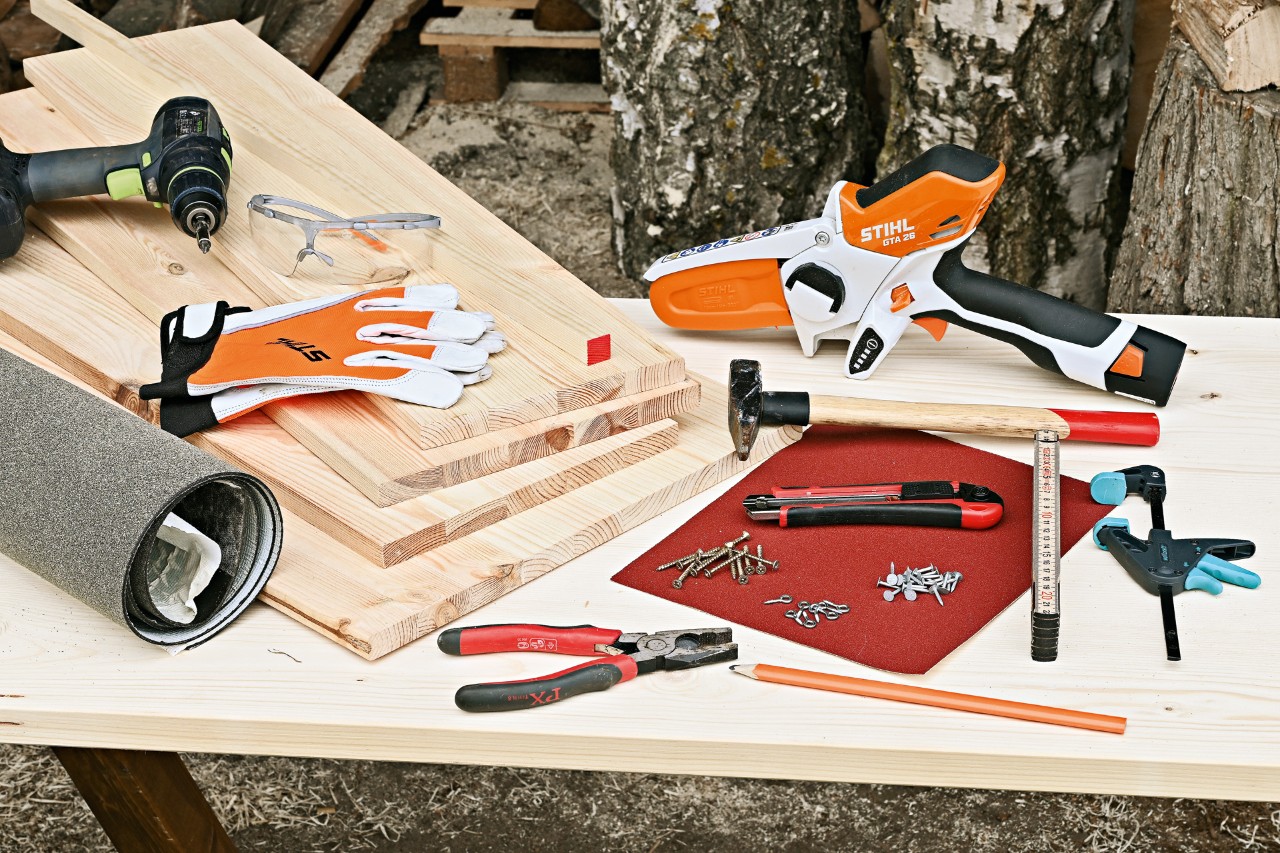 Herramientas para crear tu casa para erizos: minisierra de batería STIHL GTA 26, tablas de madera y otras herramientas.