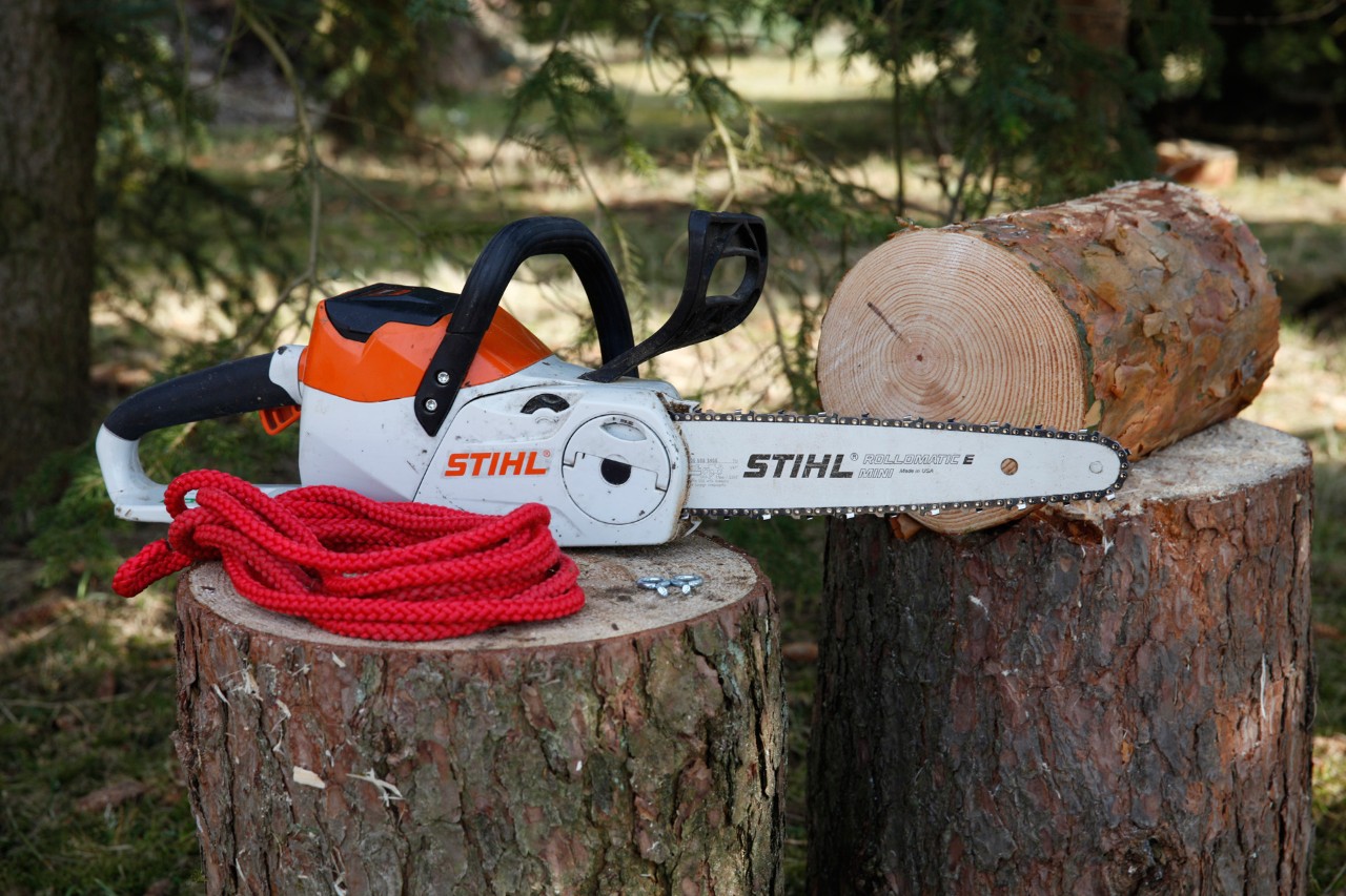 Comedero para pájaros DIY: una motosierra de batería STIHL MSA 140 C, dos cáncamos y una cuerda roja en un tronco.