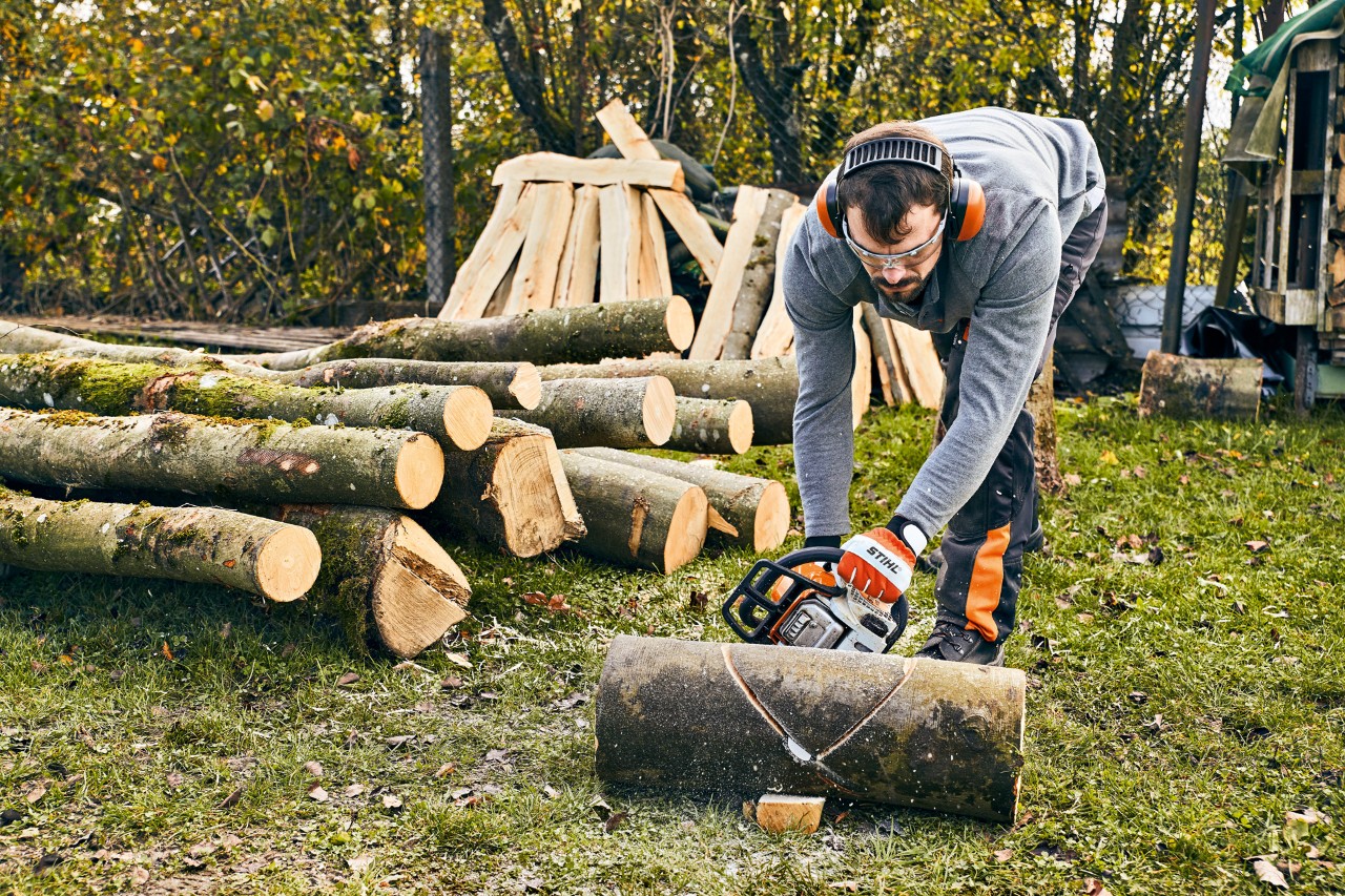 A man wearing ear protection using a STIHL MS 180 is working on a garden bench diy chainsaw is about to build a garden bench himself 