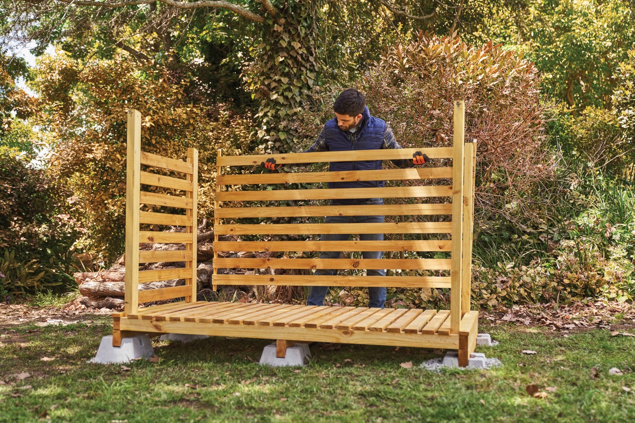 Cómo construir una leñera para exterior: un hombre montando el panel de la pared posterior para almacenar leña en casa.