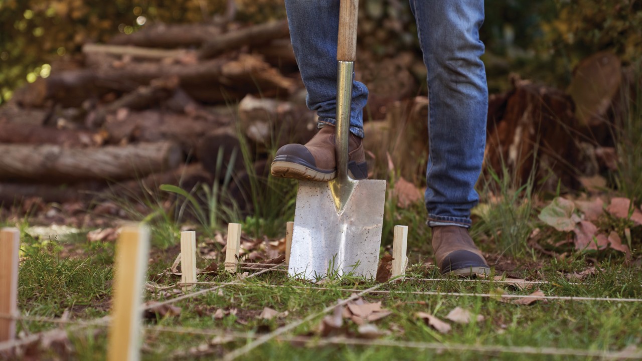 Cómo construir una leñera: primer plano de una pala insertada en el suelo y haciendo un agujero marcado con estacas.