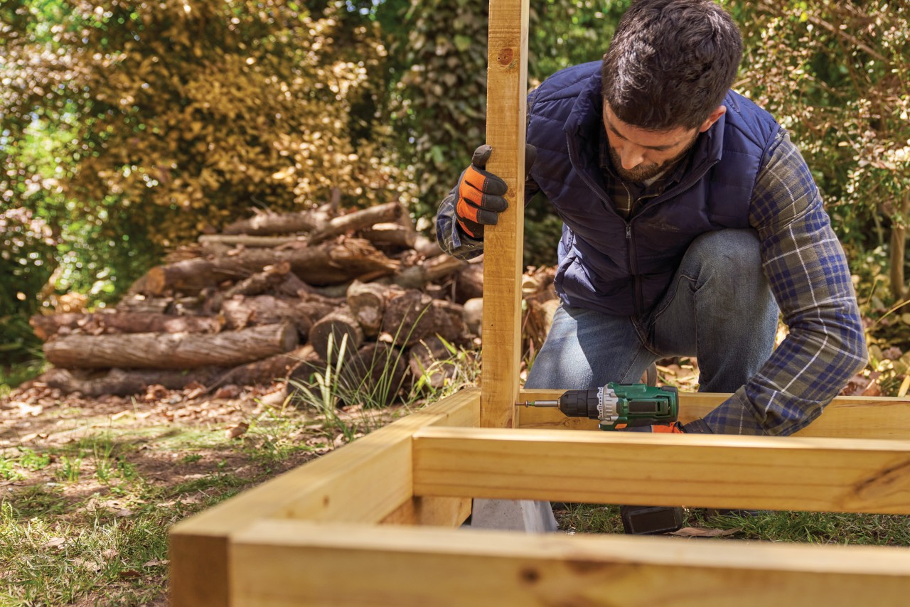 Cómo hacer un leñero de madera: un hombre fijando un montante a un marco de suelo ya construido.