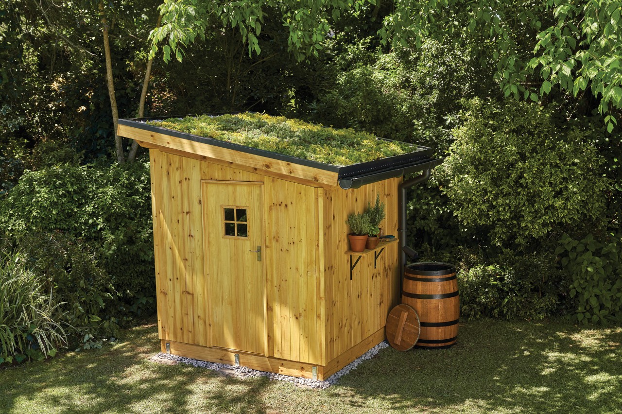 Una caseta de jardín de bricolaje con revestimiento de madera y cubierta verde.